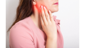brunette with pink shirt touching jaw due to TMJ pain