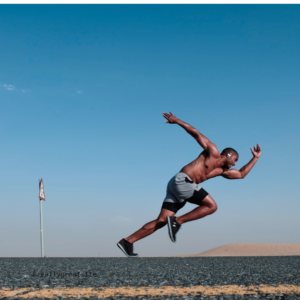 black male athlete running outdoors with athletic stance and blue skies behind him